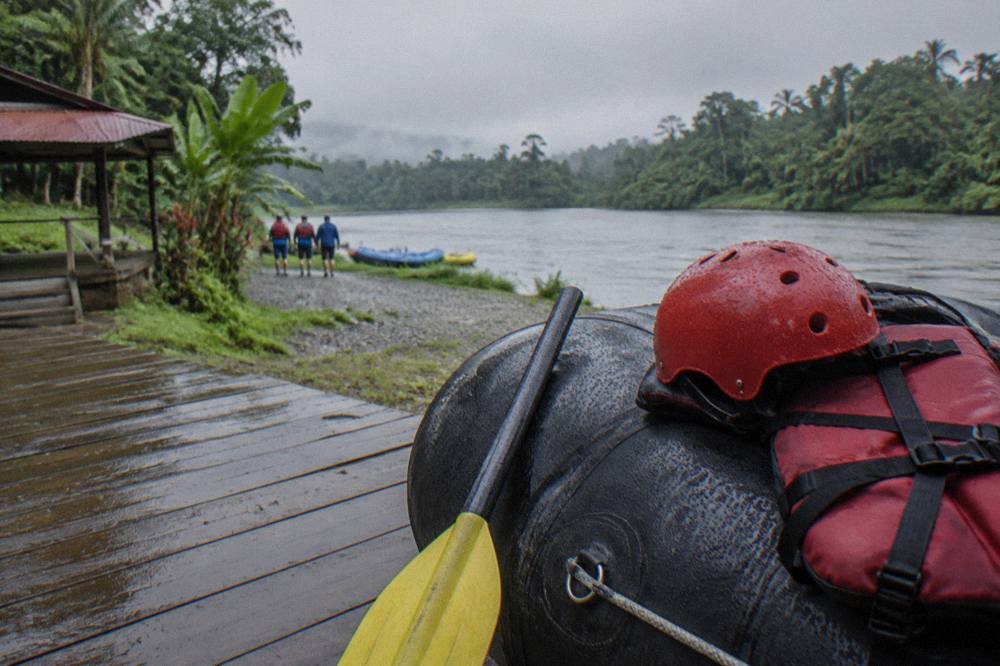 A safety helmet and life jacket resting on a raft tube beside a paddle