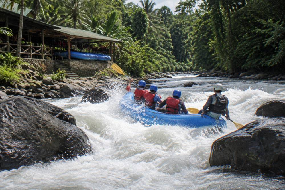 A raft paddling through a steep rapid with white waves in jungle surroundings