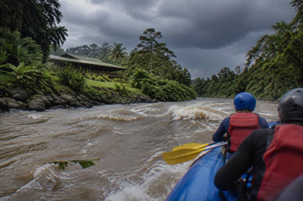An inflatable raft entering a line of whitewater waves between dense green jungle banks