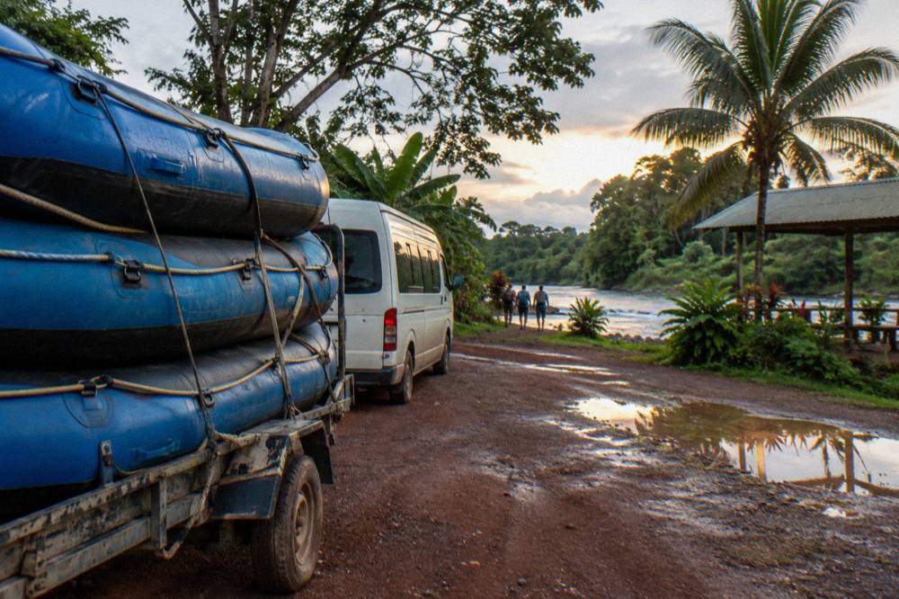 Tour van parked on a jungle road beside rafts strapped to a trailer