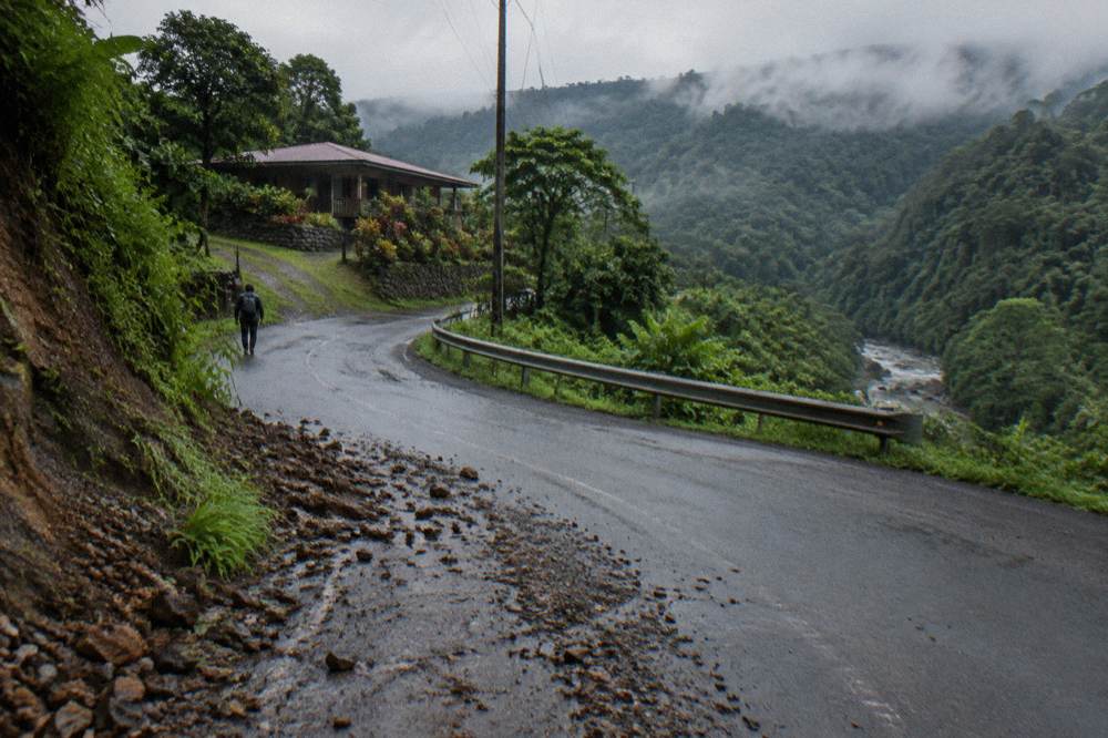 A paved mountain road curving through green hills with mist on the ridgeline