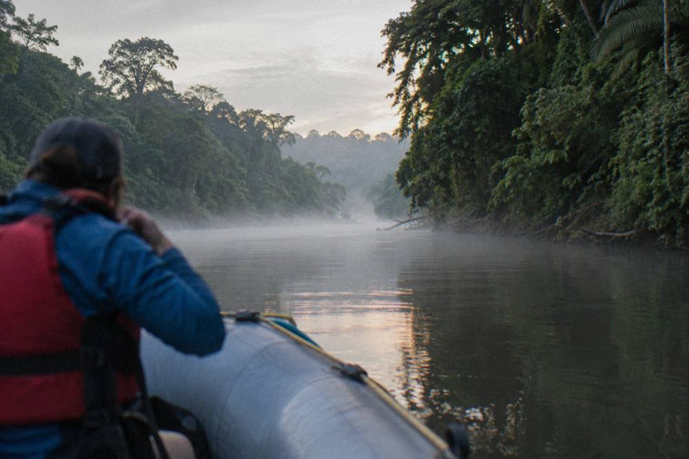 A raft floating down a calm jungle river between dense green walls of forest
