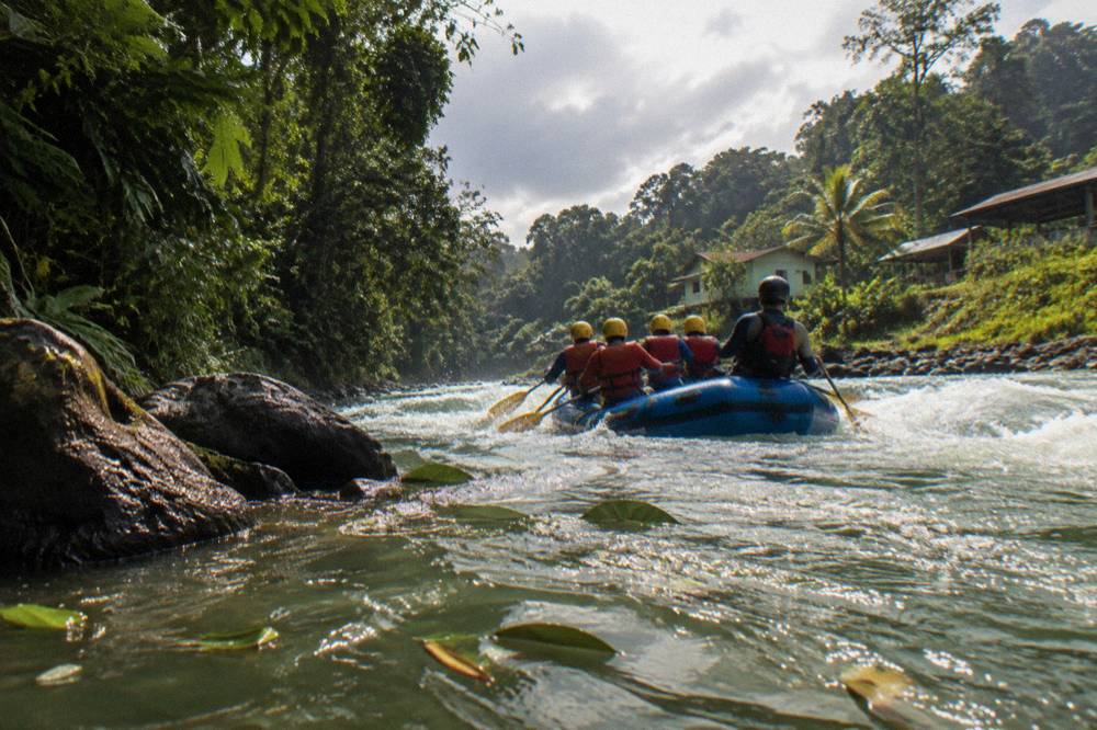 Paddlers in helmets and life jackets guiding a raft through a churning green rapid