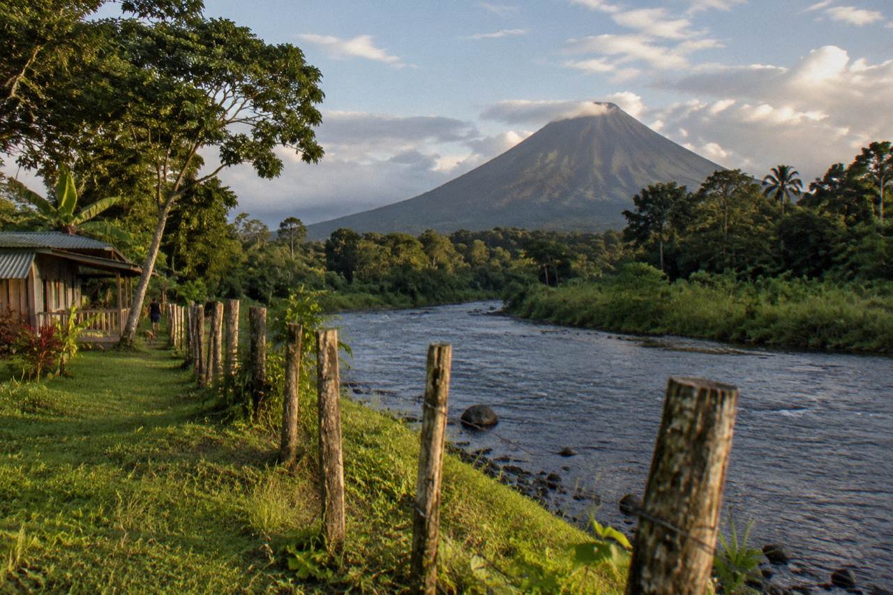A broad volcano cone rising over green forest under a partly cloudy sky