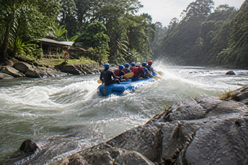 A six-person raft punching through a standing wave in a jungle rapid