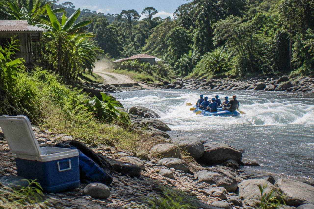 A raft cutting through a jungle rapid with spray rising over dense green forest
