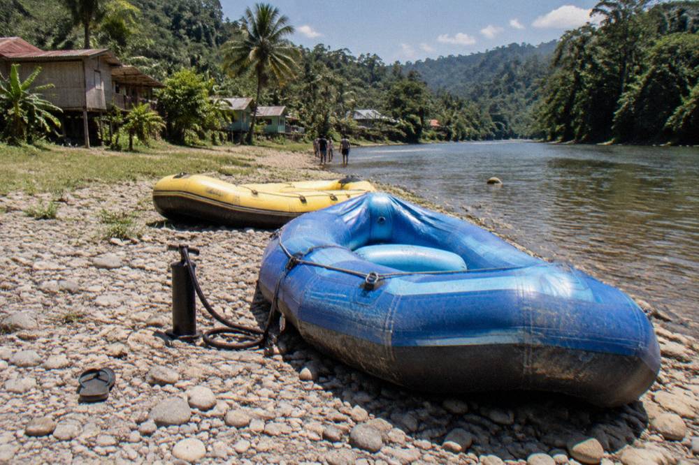Two inflatable rafts parked on a rocky riverbank beside clear tropical water