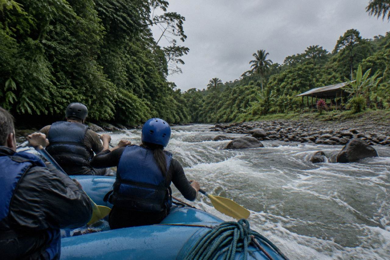 A raft cutting through a jungle rapids section under an overcast sky