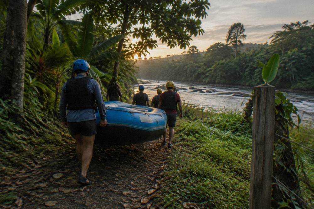 Rafters in helmets and life jackets carrying a raft toward the river through jungle