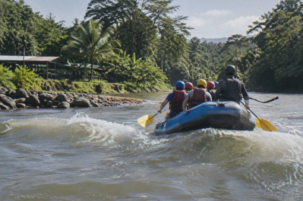 An inflatable raft cutting through a small standing wave on a tropical river