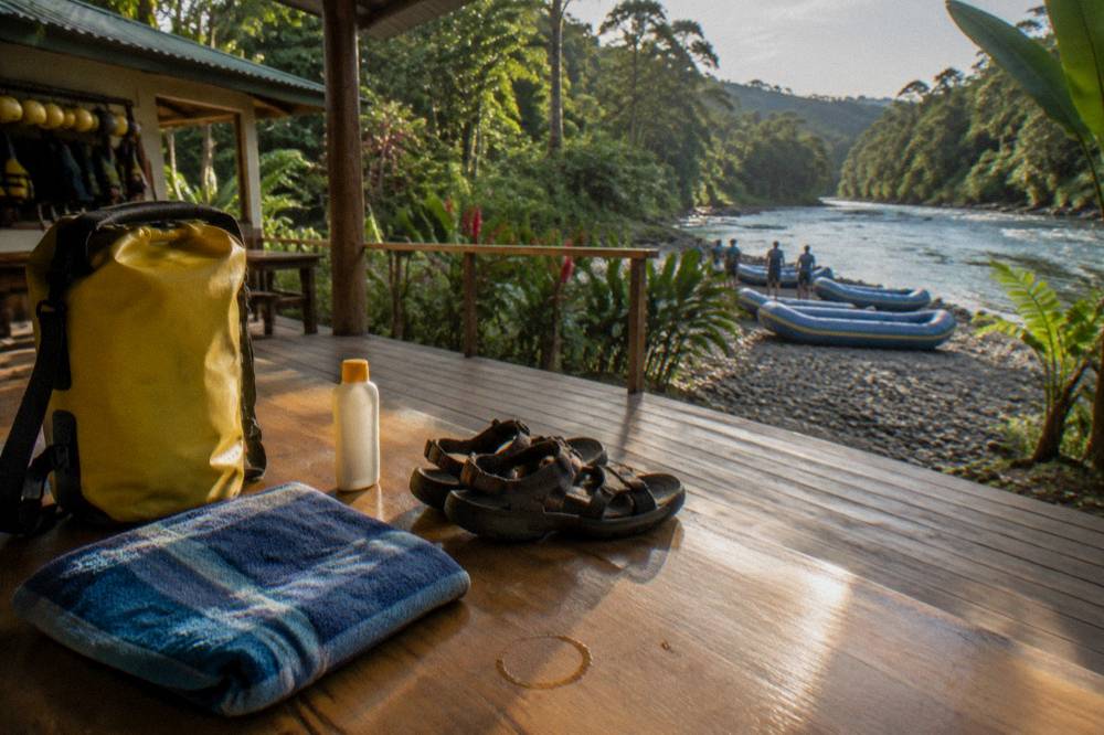 Sandals, dry bag, sunscreen and a folded towel laid out on a wooden bench