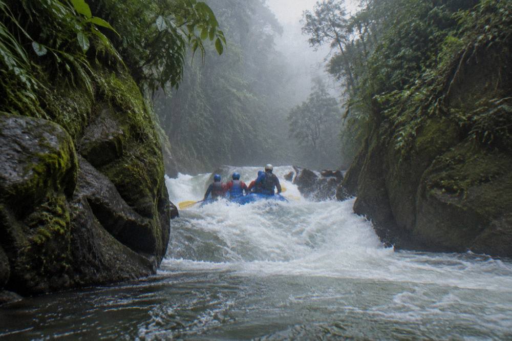 A whitewater raft plunging through a standing wave in a narrow jungle canyon