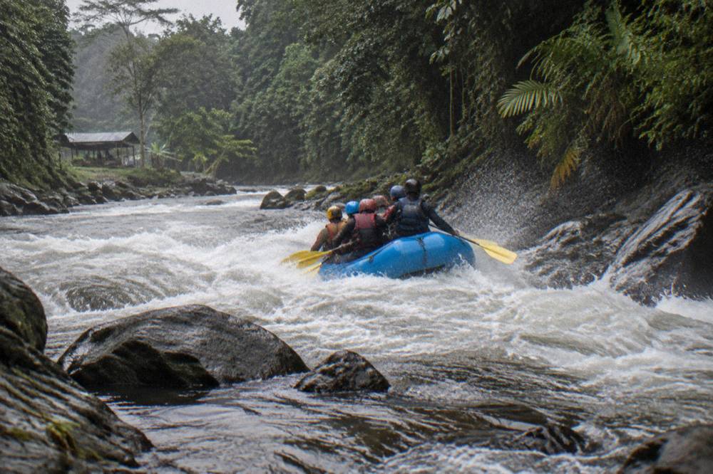 Inflatable raft paddling through a foaming whitewater rapid between jungle walls