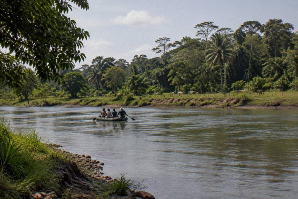 An inflatable raft carrying a small crew drifting through a wide calm jungle river bend