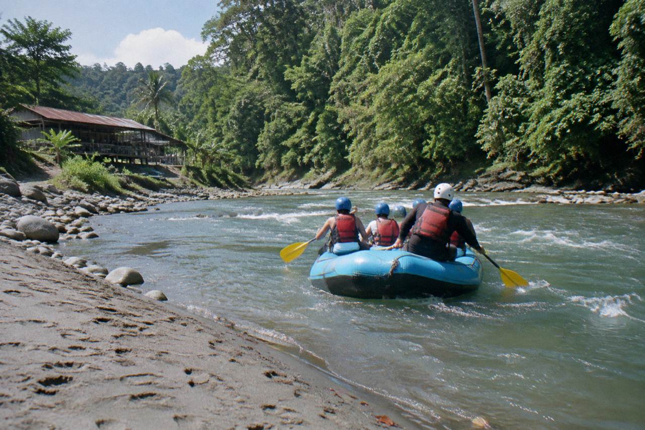 A raft with paddlers in helmets and life jackets floating through gentle green jungle rapids