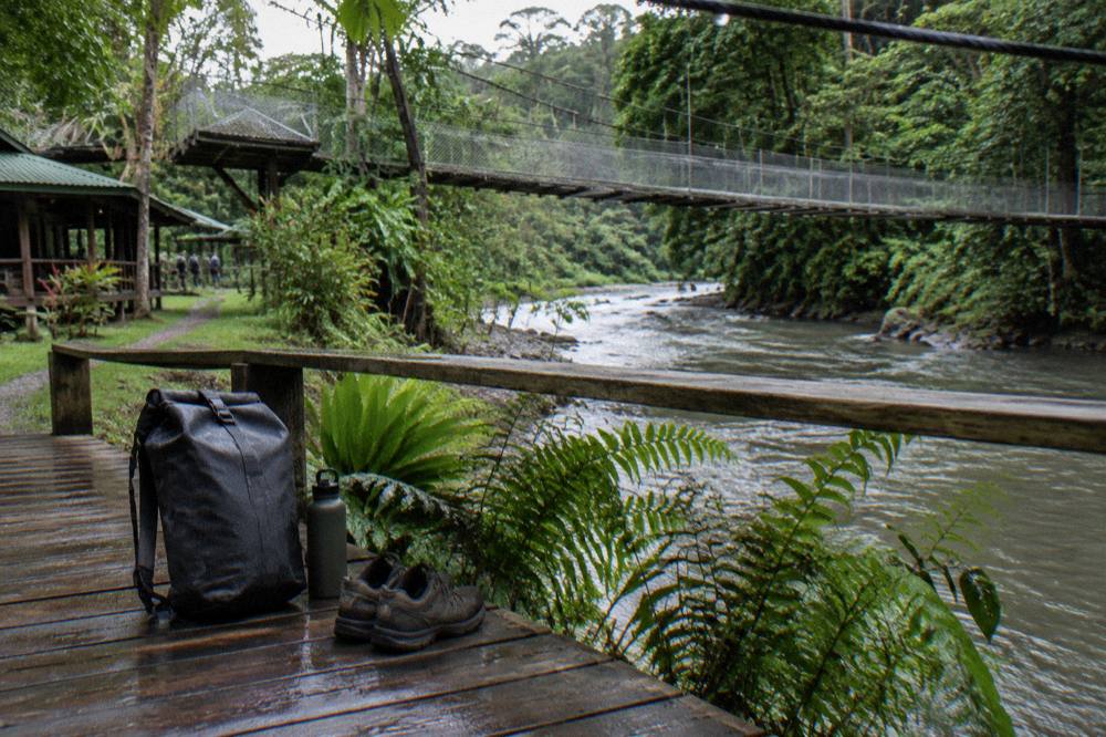 Dry bag, water bottle, sunscreen and walking shoes arranged on a wooden bench beside a river