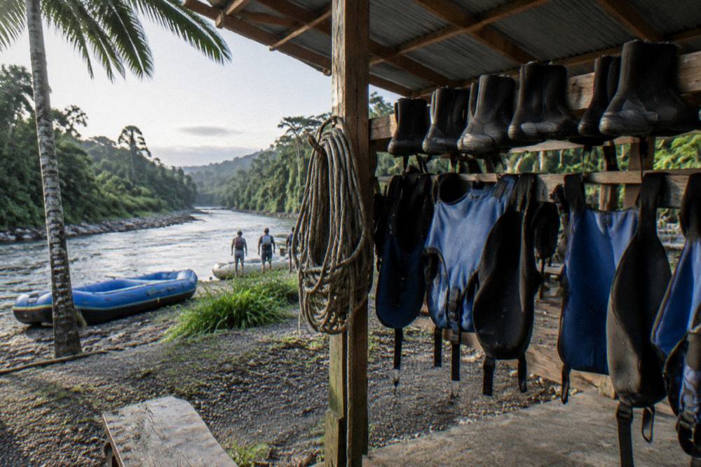 A wooden rafting base building with equipment racks and rafting gear drying in the shade