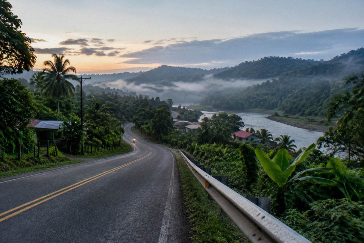 A quiet two-lane road winding through green rainforest hills toward the Sarapiqui lowlands