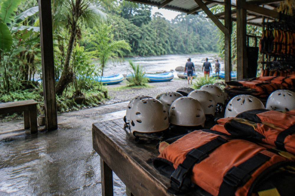 A close view of whitewater helmets and orange life vests laid out on a riverside bench