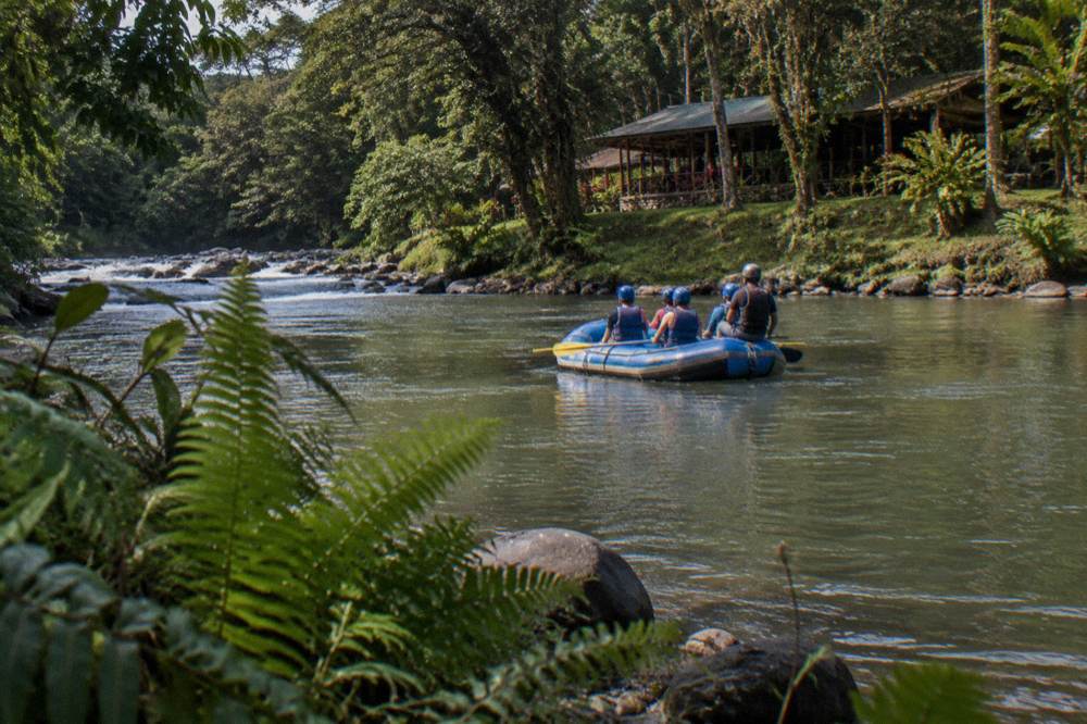A family in helmets and vests sitting in a raft on calm jungle water between rapids