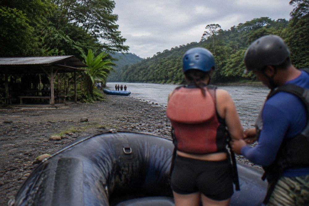 Guide adjusting the straps of a life jacket on a rafting guest at a river put-in