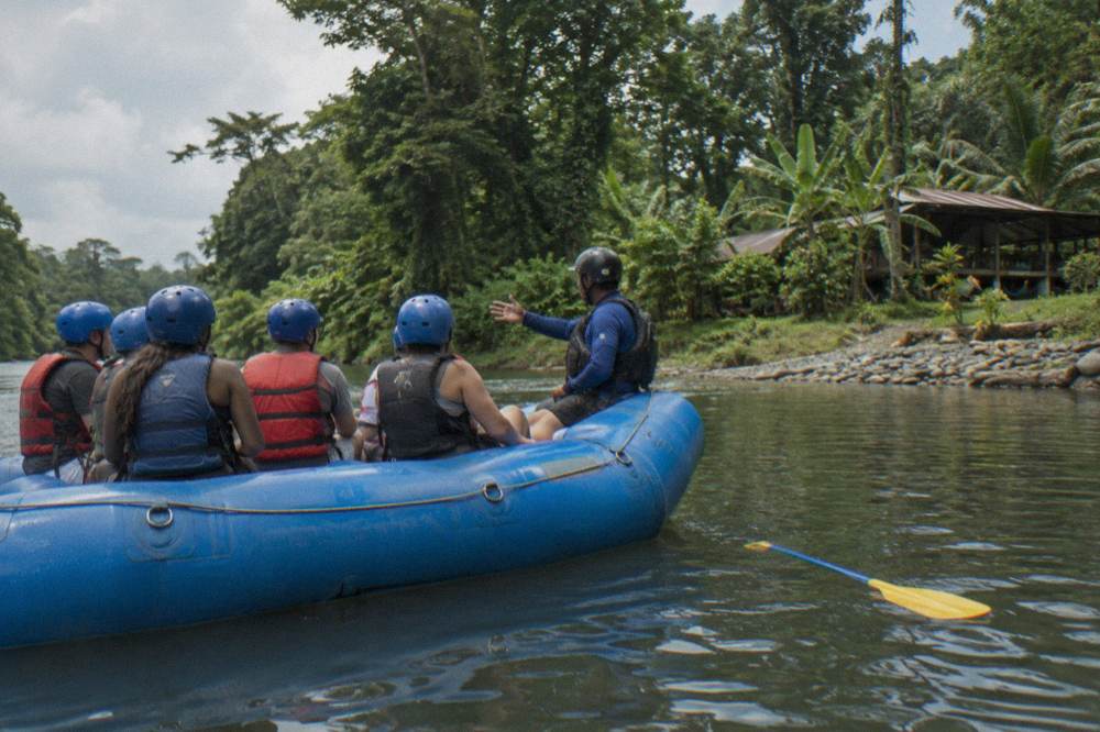 Rafting guests seated in a raft wearing helmets and life jackets listening to a safety briefing