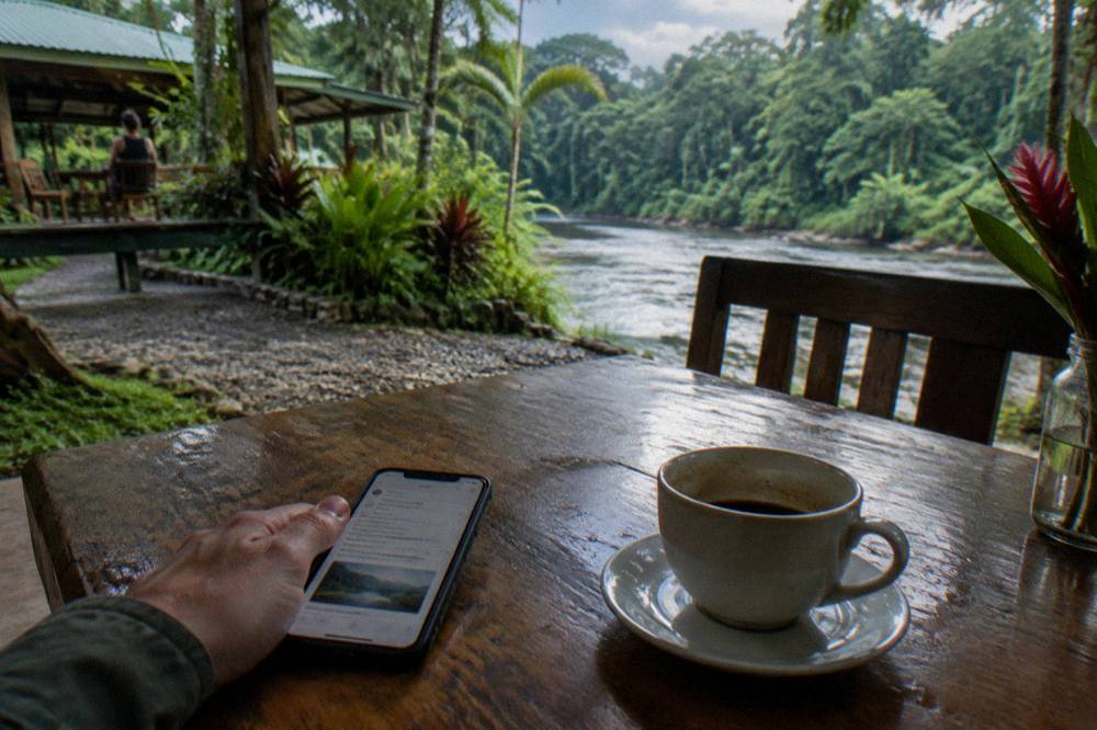Booking confirmation on a phone held by a traveler at a wooden riverside table