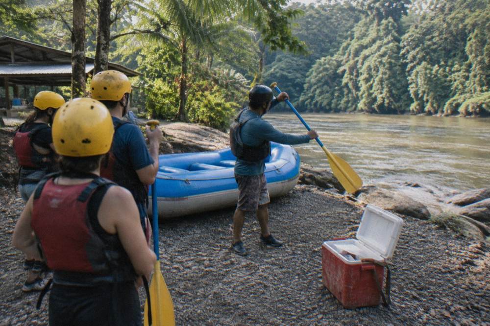 A guide instructing paddlers wearing helmets and life jackets beside an inflatable raft