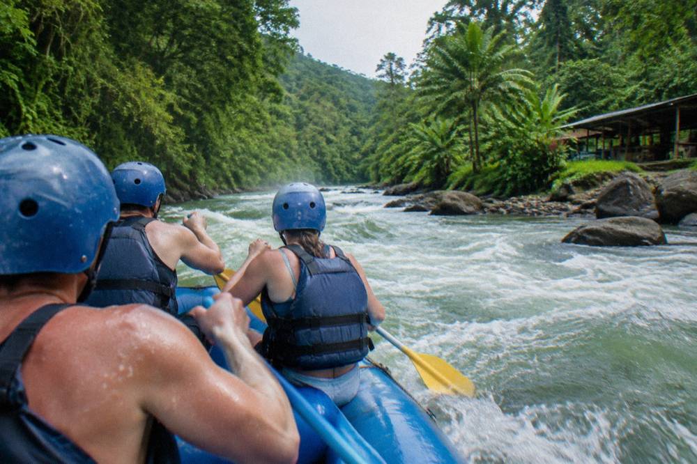 A raft paddling through a foamy green rapid between jungle walls