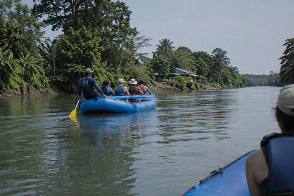 A guide giving paddling instructions to a raft crew on a wide green river