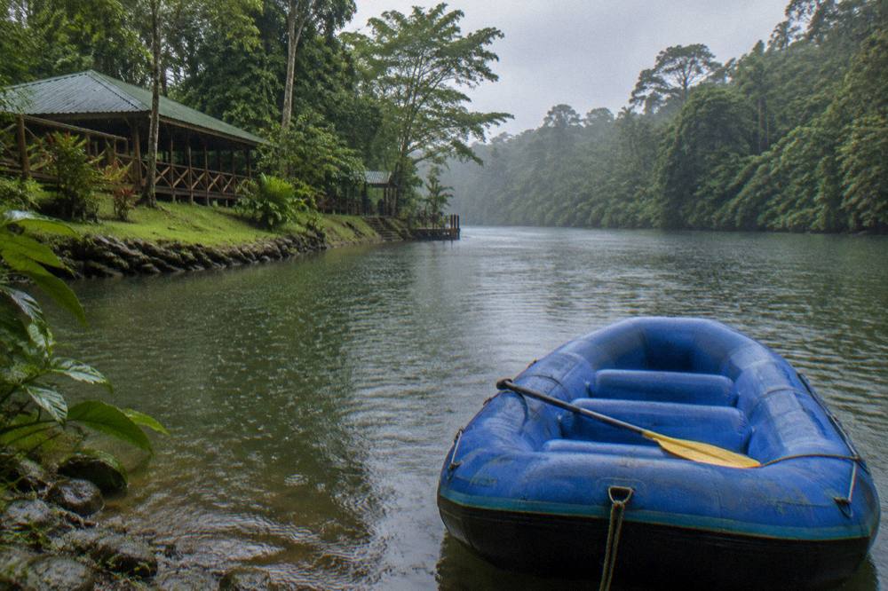 An empty raft floating on calm green water between rainforest banks in soft rain