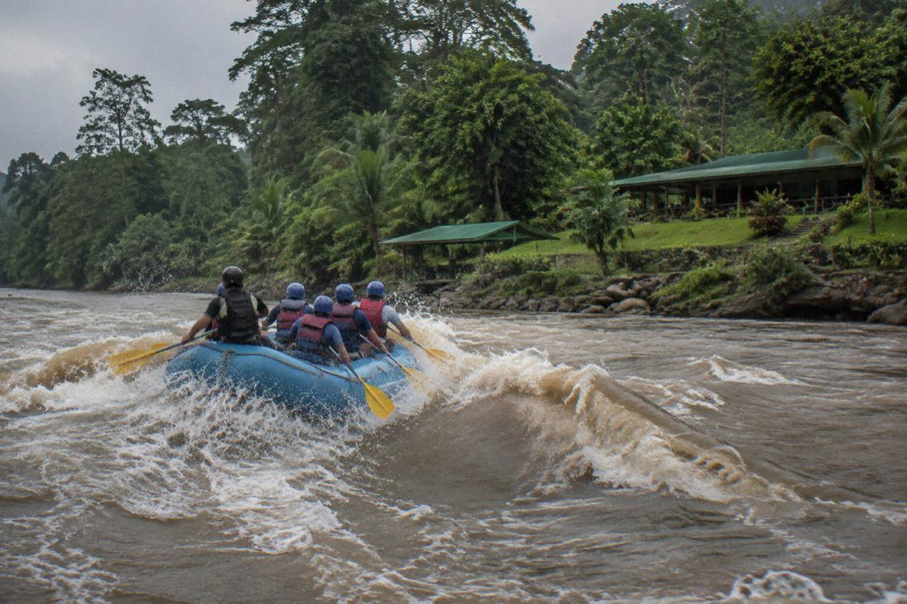 A raft cutting through a green jungle rapid on the Sarapiqui River under an overcast sky