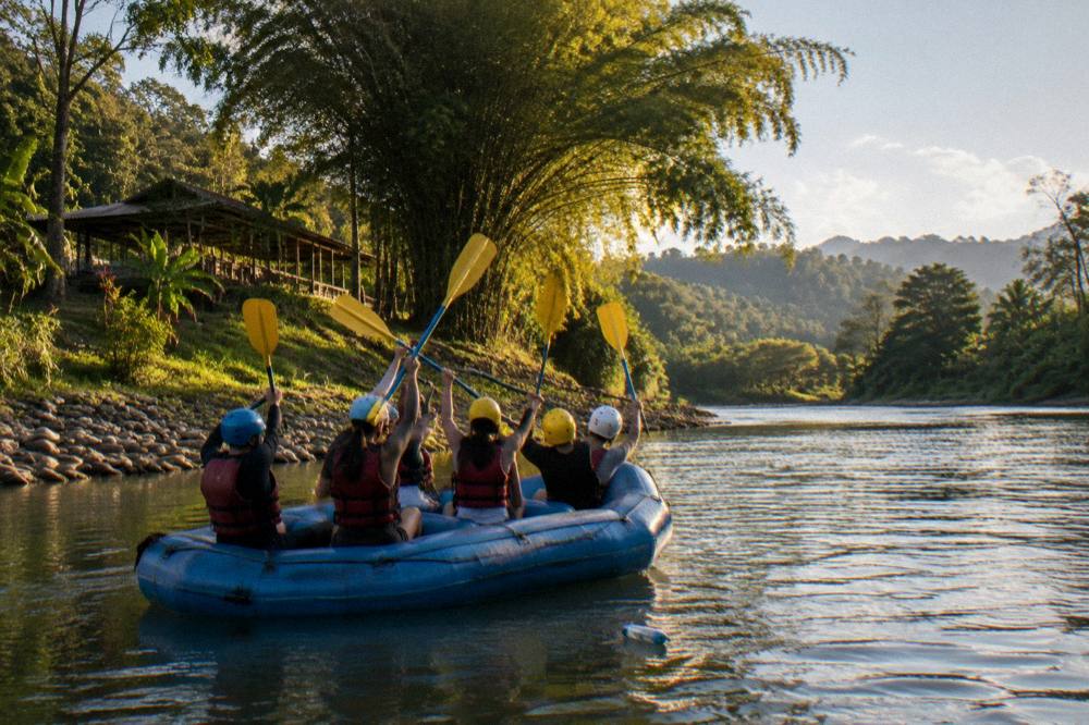 A raft team celebrating with raised paddles on a calm jungle river stretch