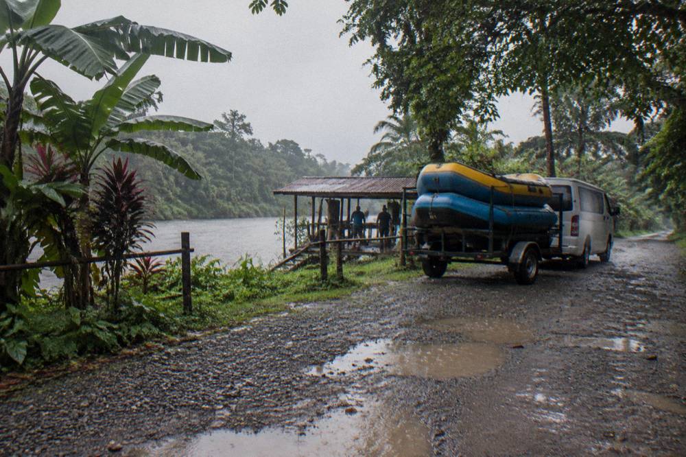 A van and trailer with rafts parked on a rural road beside rainforest