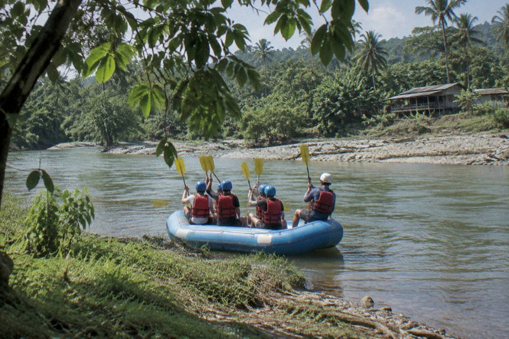 A family in helmets and life jackets smiling in a raft on calm water