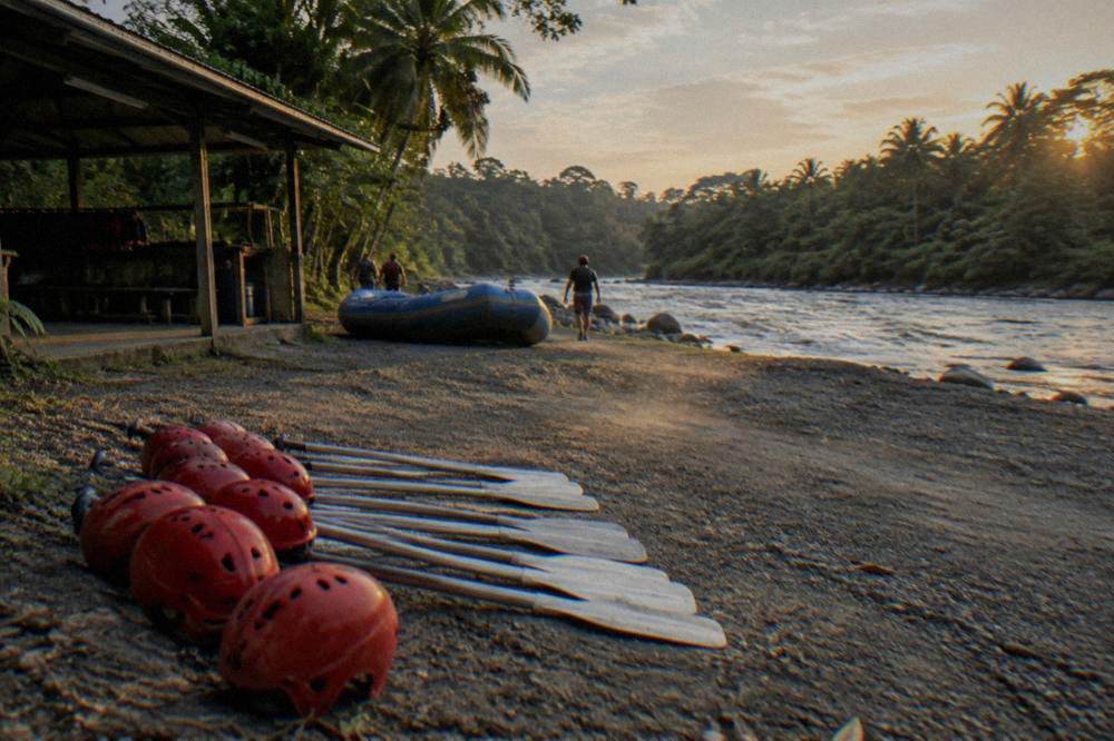 Rafting paddles and helmets laid out on a riverbank