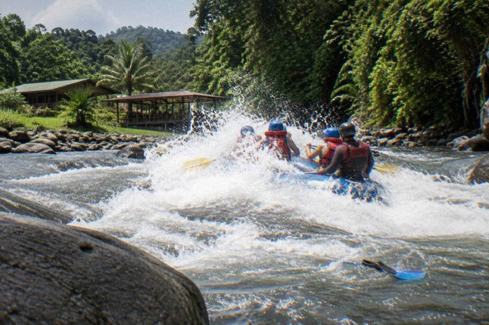 Raft plunging through a whitewater wave with paddlers bracing as spray rises over the bow
