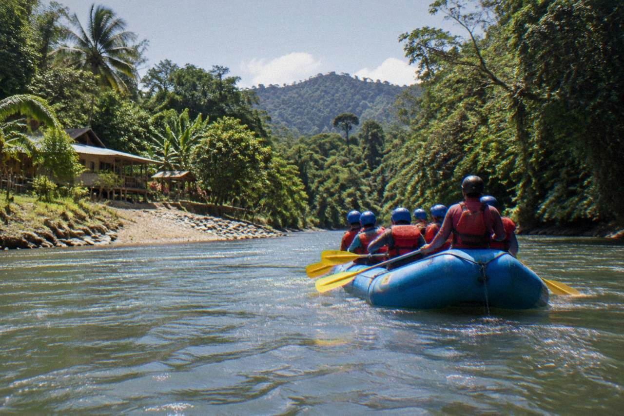 Inflatable raft with paddlers in helmets and life jackets on a jungle river with dense green forest on both banks