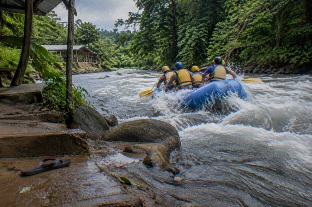 A raft with paddlers cutting through a splashing rapid between forested banks