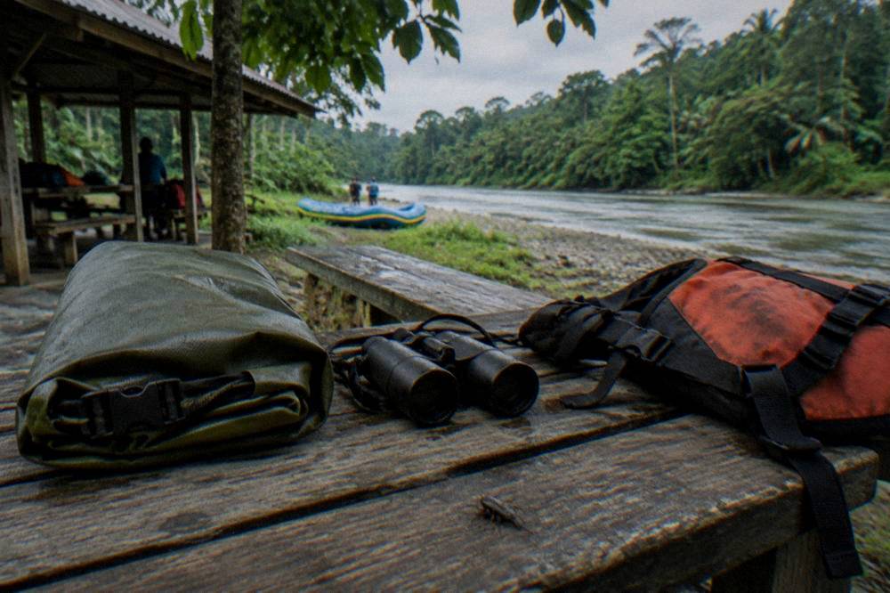 A dry bag and binoculars resting on a wooden bench beside a life jacket