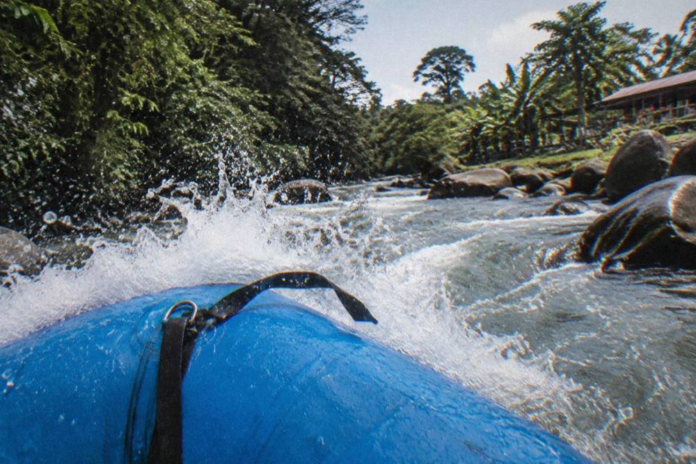 Whitewater waves breaking over the bow of a raft in a narrow jungle river channel