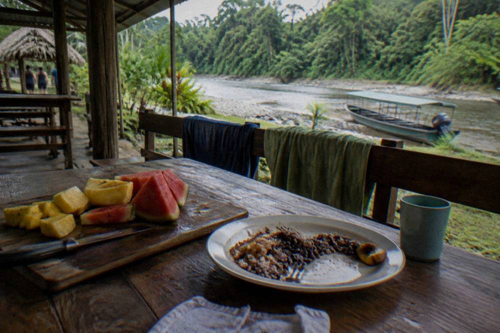 A spread of tropical fruit and a prepared lunch on a table at a riverbase shelter