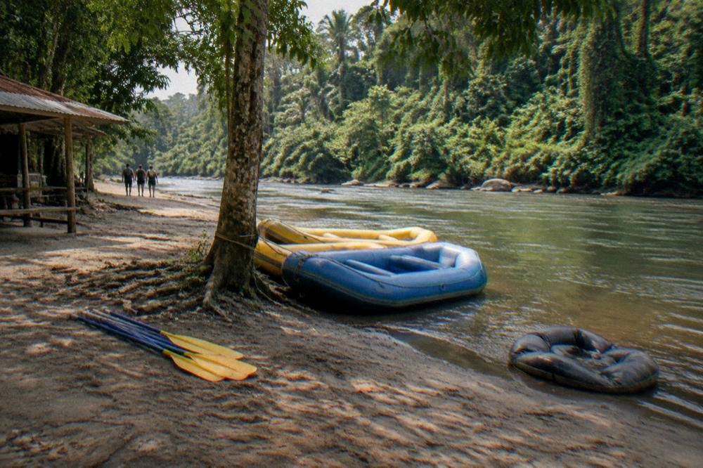 Two rafts tied at a riverside takeout with paddles stacked and rainforest behind