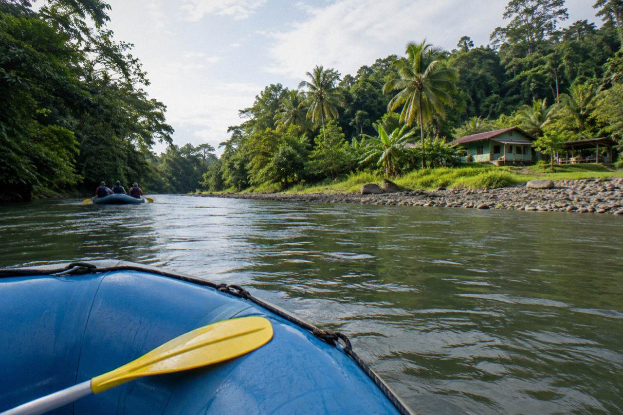 A raft floating through green jungle along a wide tropical river bend