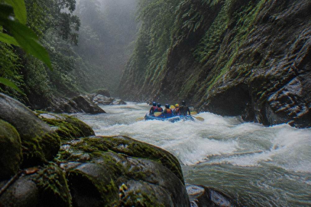 A raft mid-rapid with white waves and steep forested canyon walls behind it
