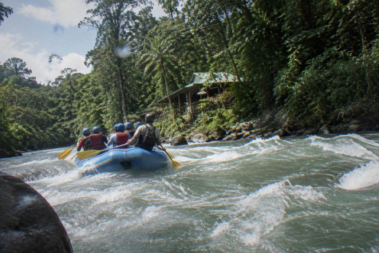 A raft cutting through a jungle rapid on a wide tropical river at midday