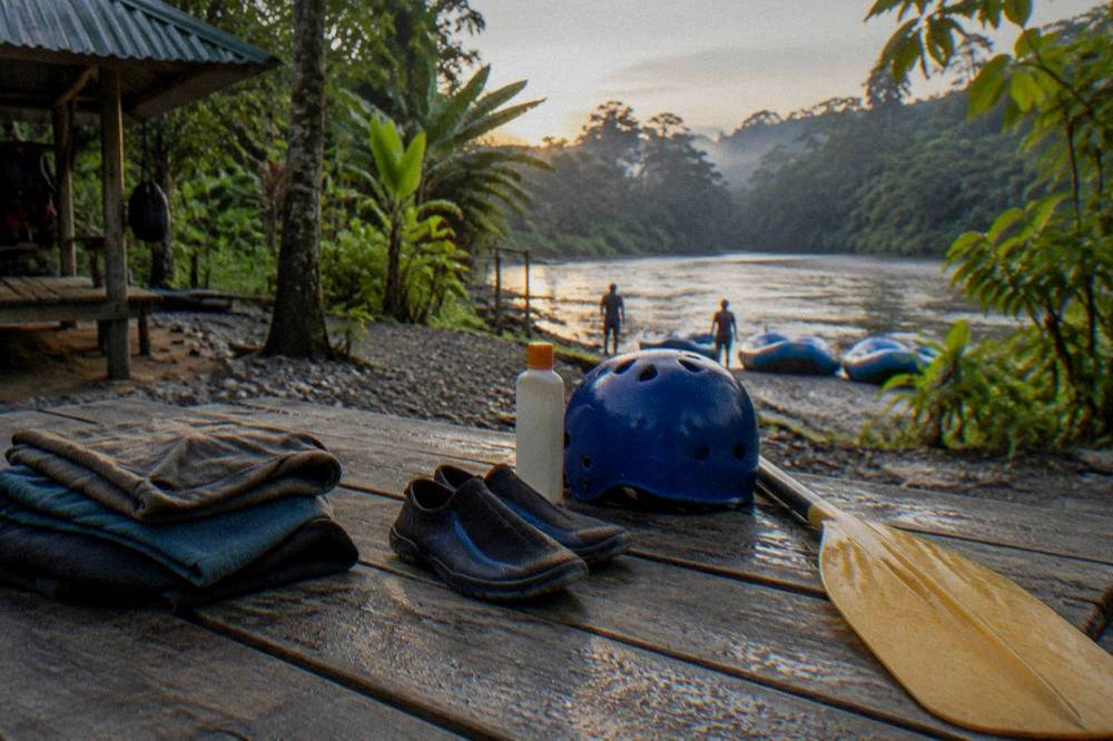 Dry clothes, water shoes and sunscreen laid out on a bench beside a paddle and helmet.