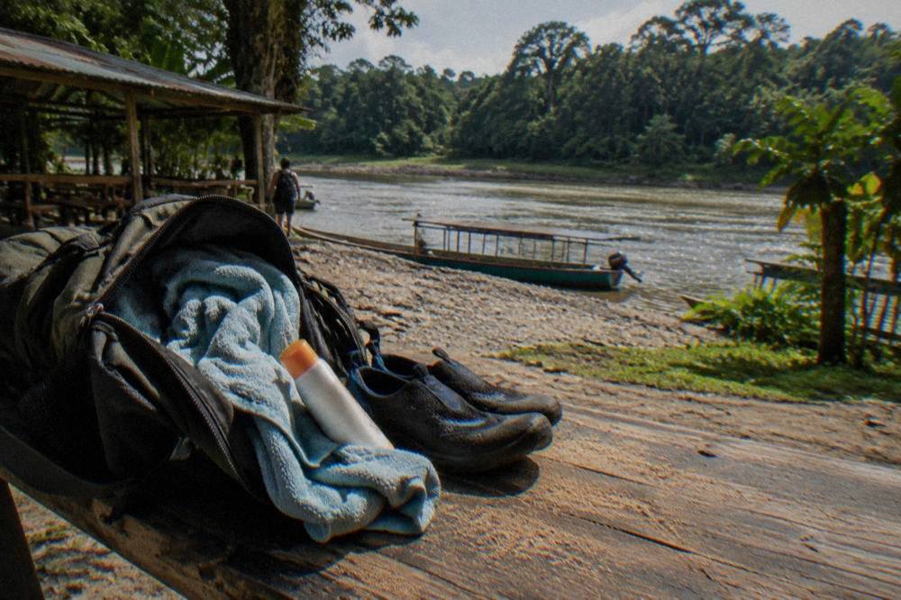 A daypack with a towel, water shoes and sunscreen open on a wooden bench at a rafting base