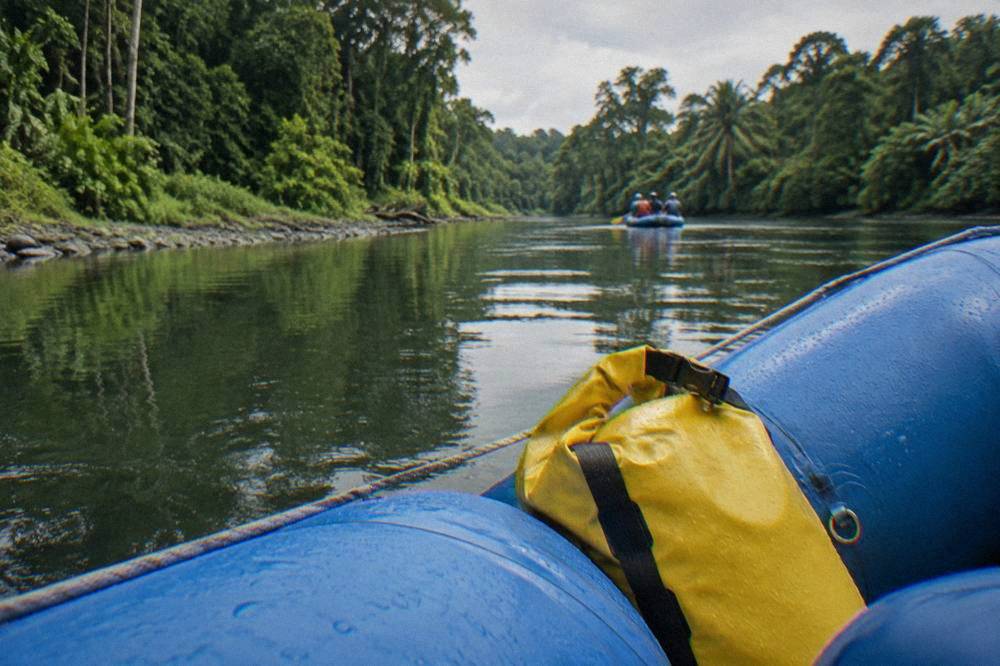 A sealed dry bag resting between the tubes of an inflated raft on a jungle river