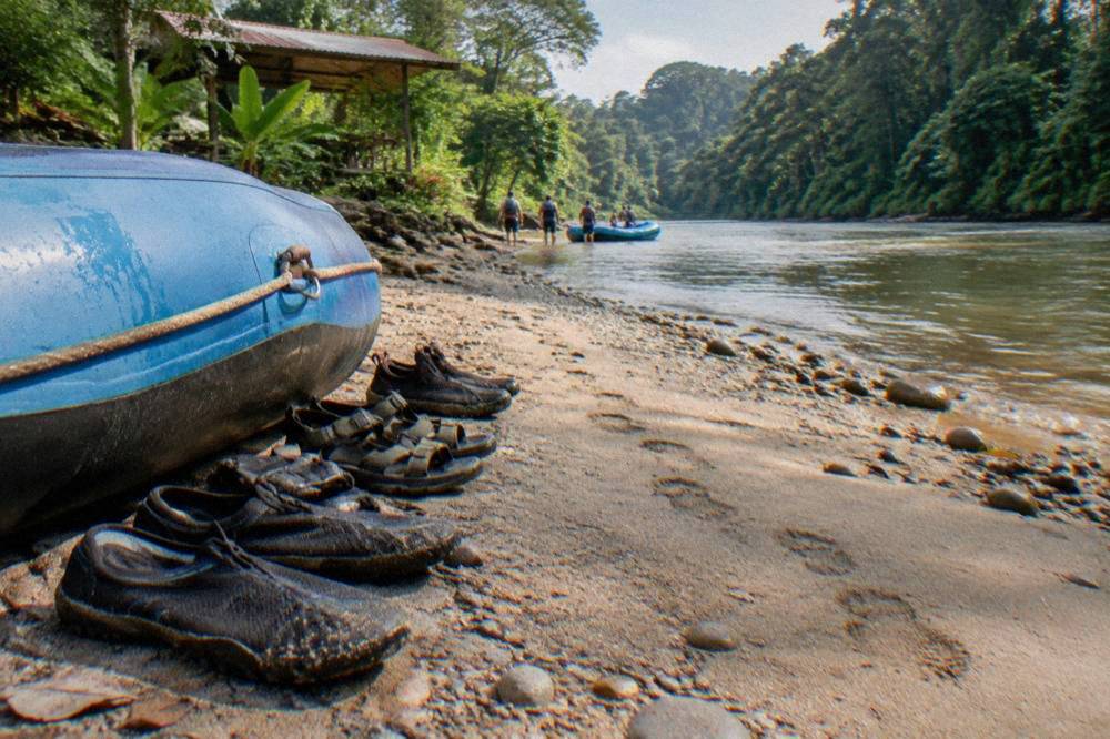 Strapped sandals and water shoes lined up beside a raft on a gravel riverbank